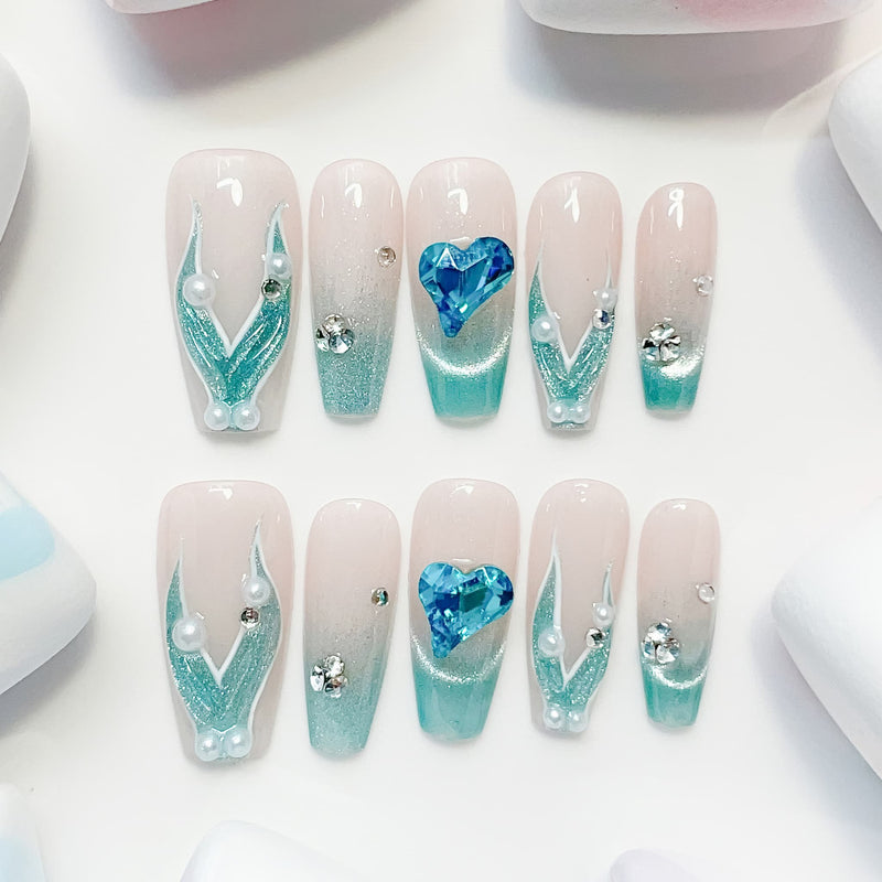 A set of false nails showcasing a mermaid-inspired design with teal colors and glossy finish