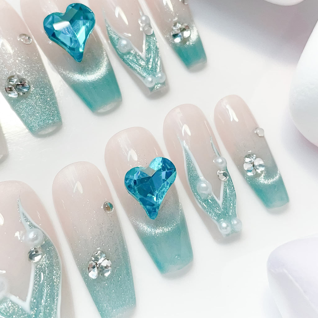 A set of false nails showcasing a mermaid-inspired design with teal colors and glossy finish