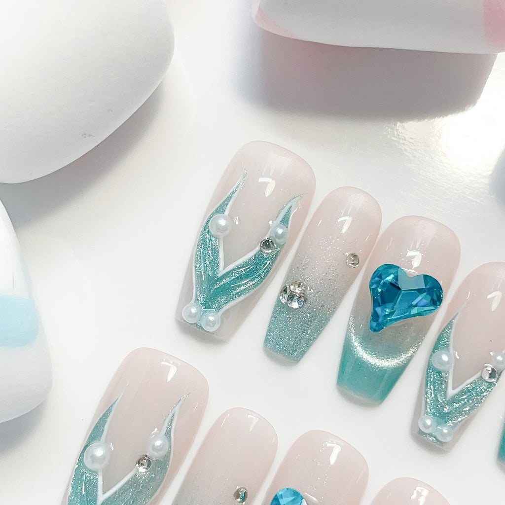 A set of false nails showcasing a mermaid-inspired design with teal colors and glossy finish