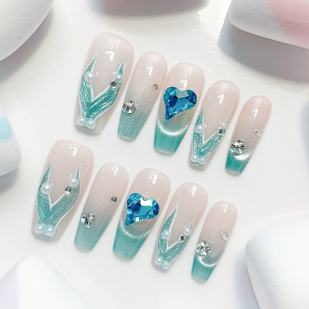 A set of false nails showcasing a mermaid-inspired design with teal colors and glossy finish
