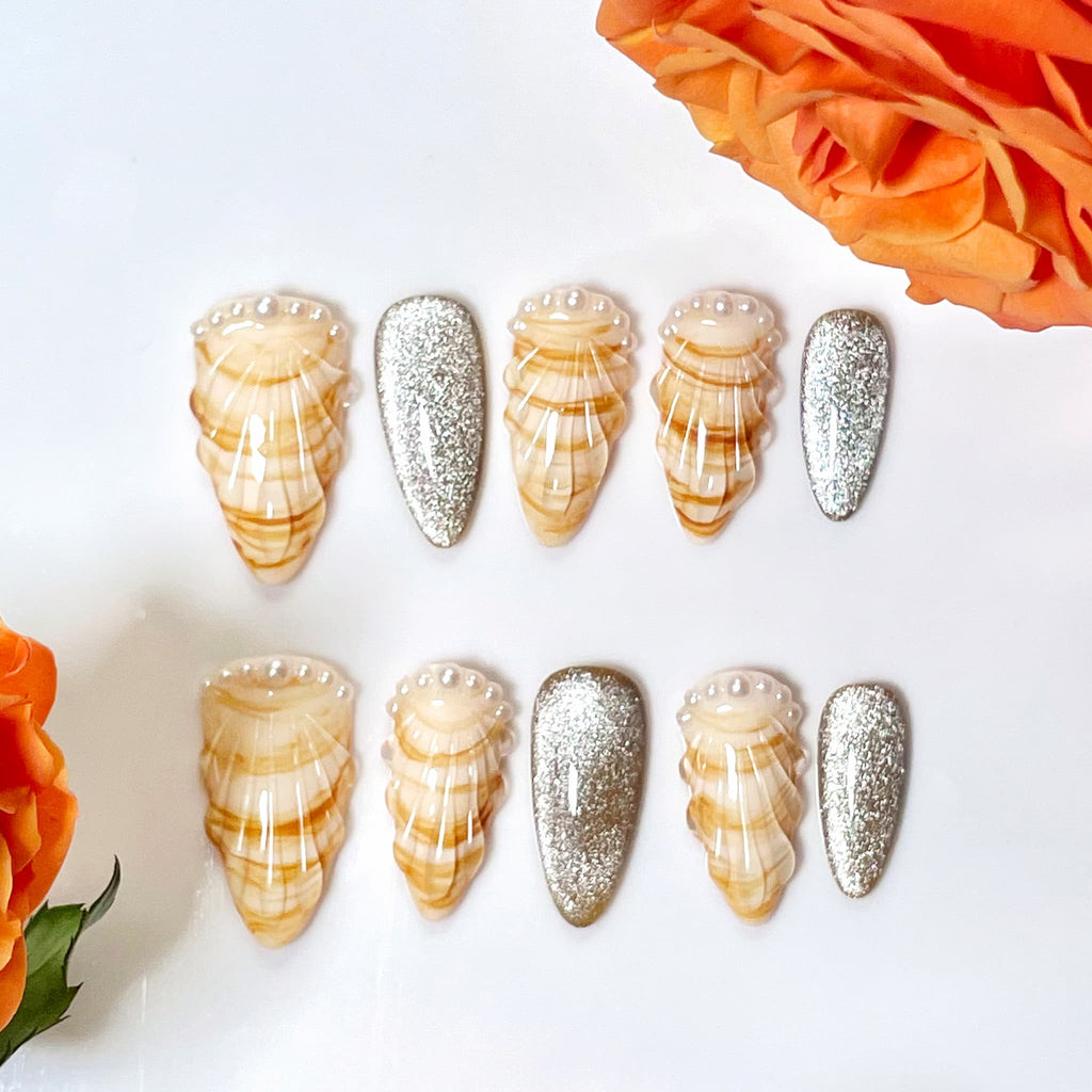 medium length gold almond press on nails with seashell designs and silver glitters